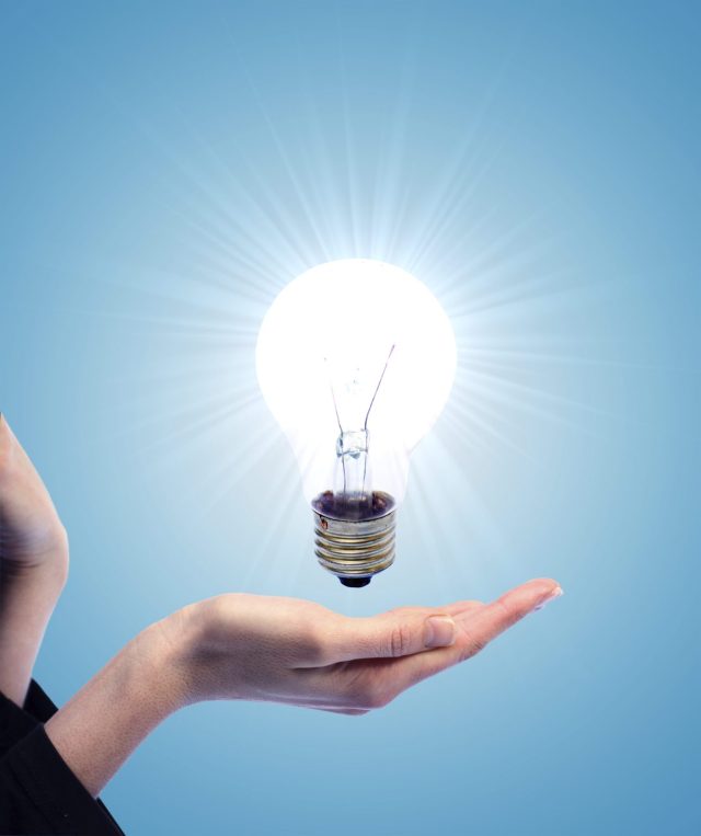 OPTIMISER L'ECLAIRAGE DE SON GARAGE Main tenant une ampoule illuminée au-dessus de sa main, représentant une idée brillante.