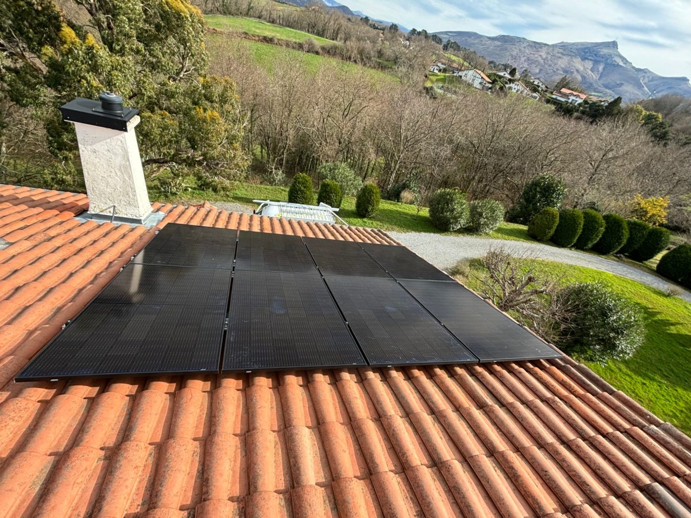 Installation de panneaux solaires Toit en tuiles avec un panneau solaire, surplombant un jardin verdoyant et des collines.
