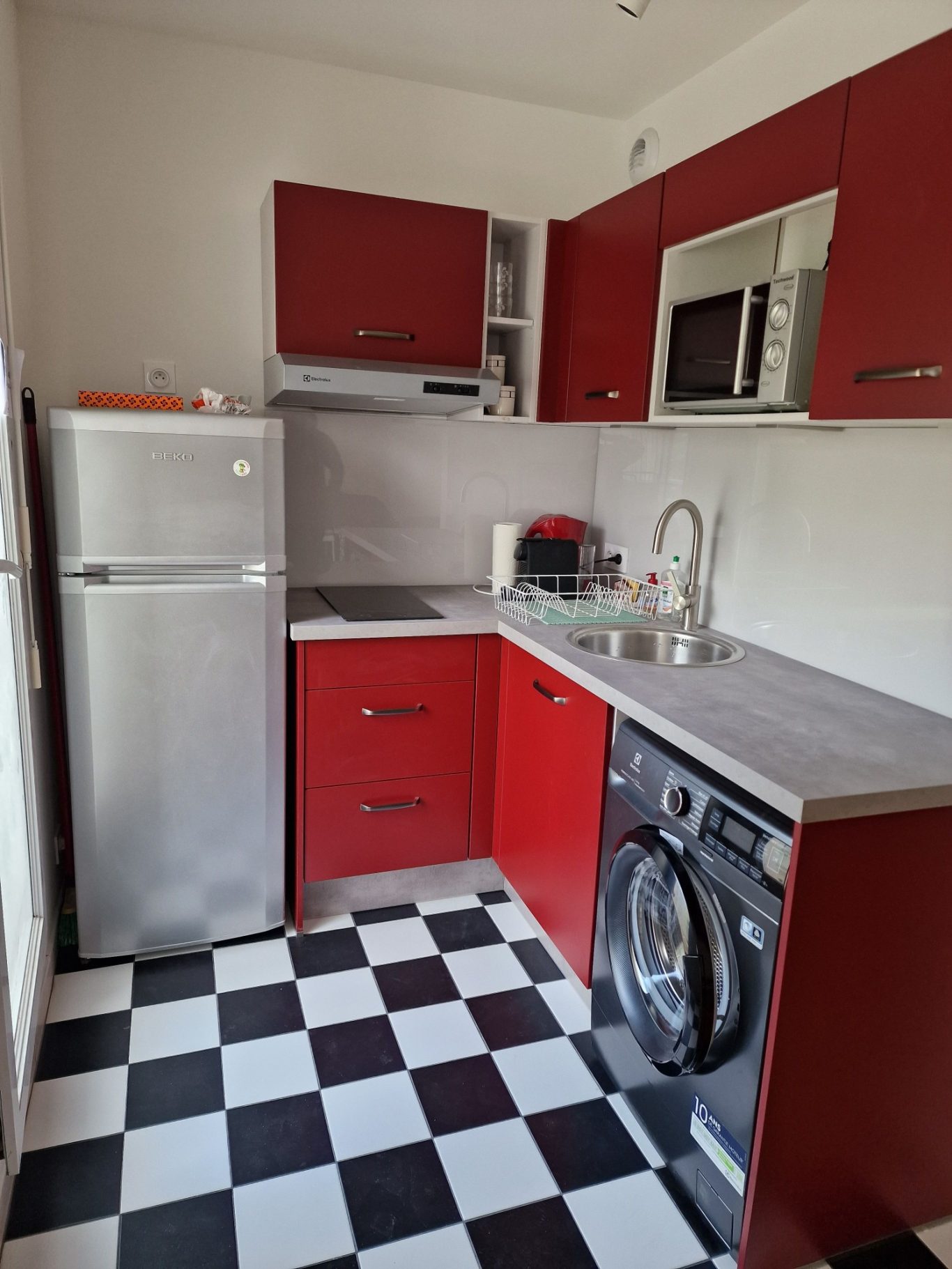 AMÉNAGEMENT D'UNE CUISINE POUR CRÉER UNE NOUVELLE PIÈCE DE RANGEMENT Cuisine moderne avec des meubles rouges, un réfrigérateur, un micro-ondes et un lave-linge.