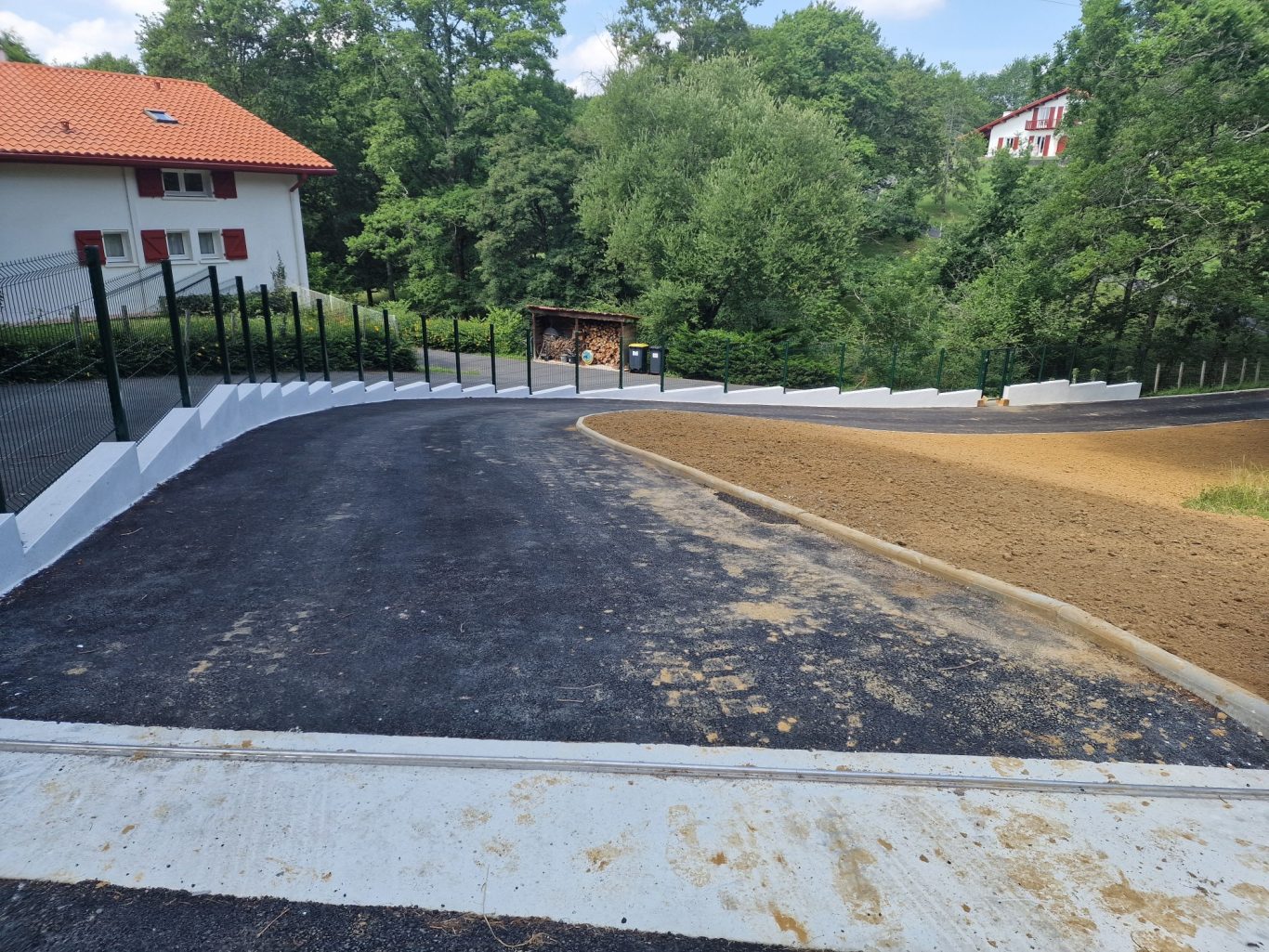 Création d'un portail et d'une allée Chemin en courbe, avec une partie asphaltée et une autre en terre, entouré d'arbres.