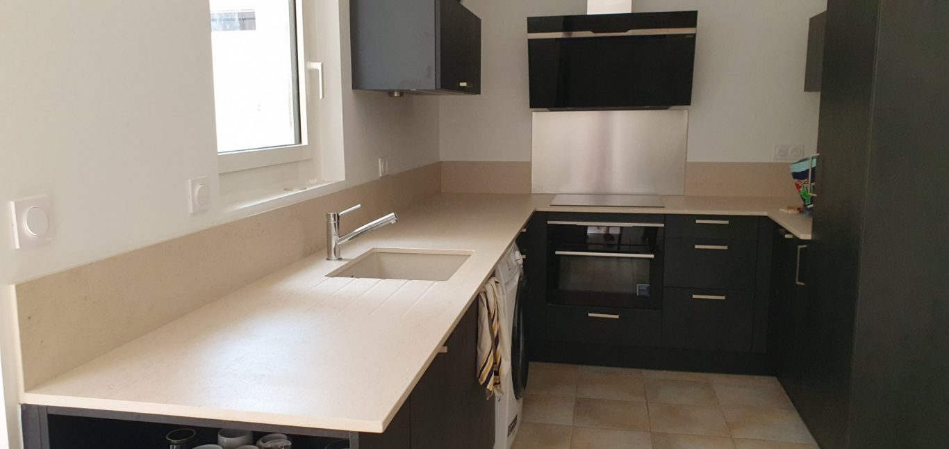 Rénovation cuisine Cuisine moderne avec des armoires noires et comptoir clair, équipée de divers appareils.