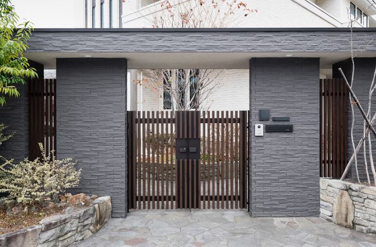 PORTAIL BATTANT OU COULISSANT : QUE CHOISIR ? Portail en bois foncé entouré de murs en pierre grise et végétation.