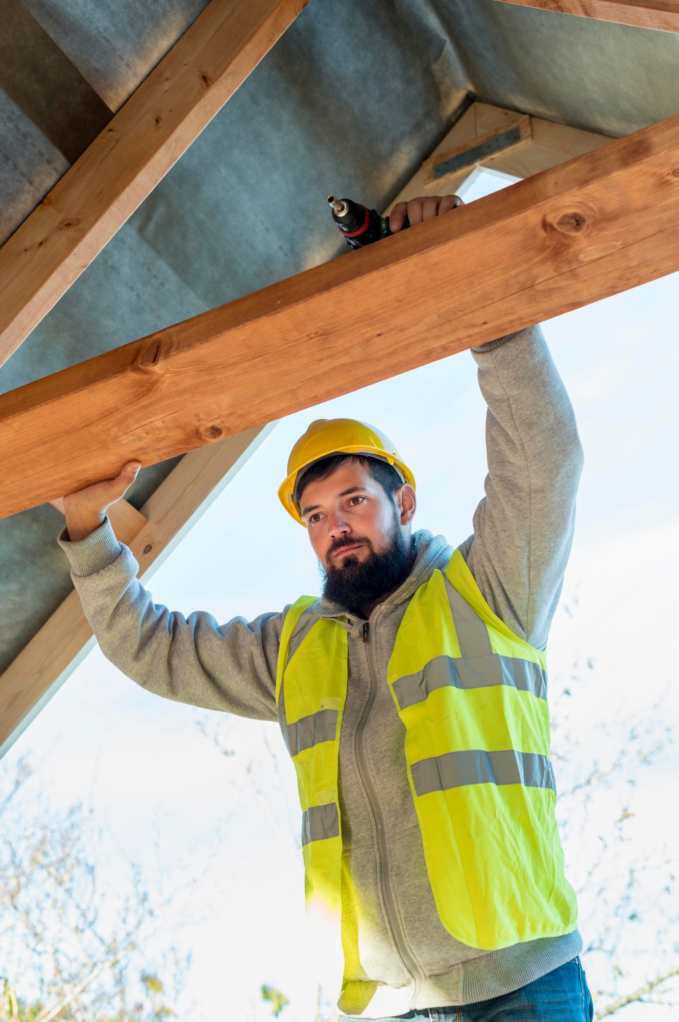 LES ERREURS A EVITER LORS DE LA SURELEVATION DE MAISON Homme en gilet de sécurité et casque, travaillant sur une structure en bois.